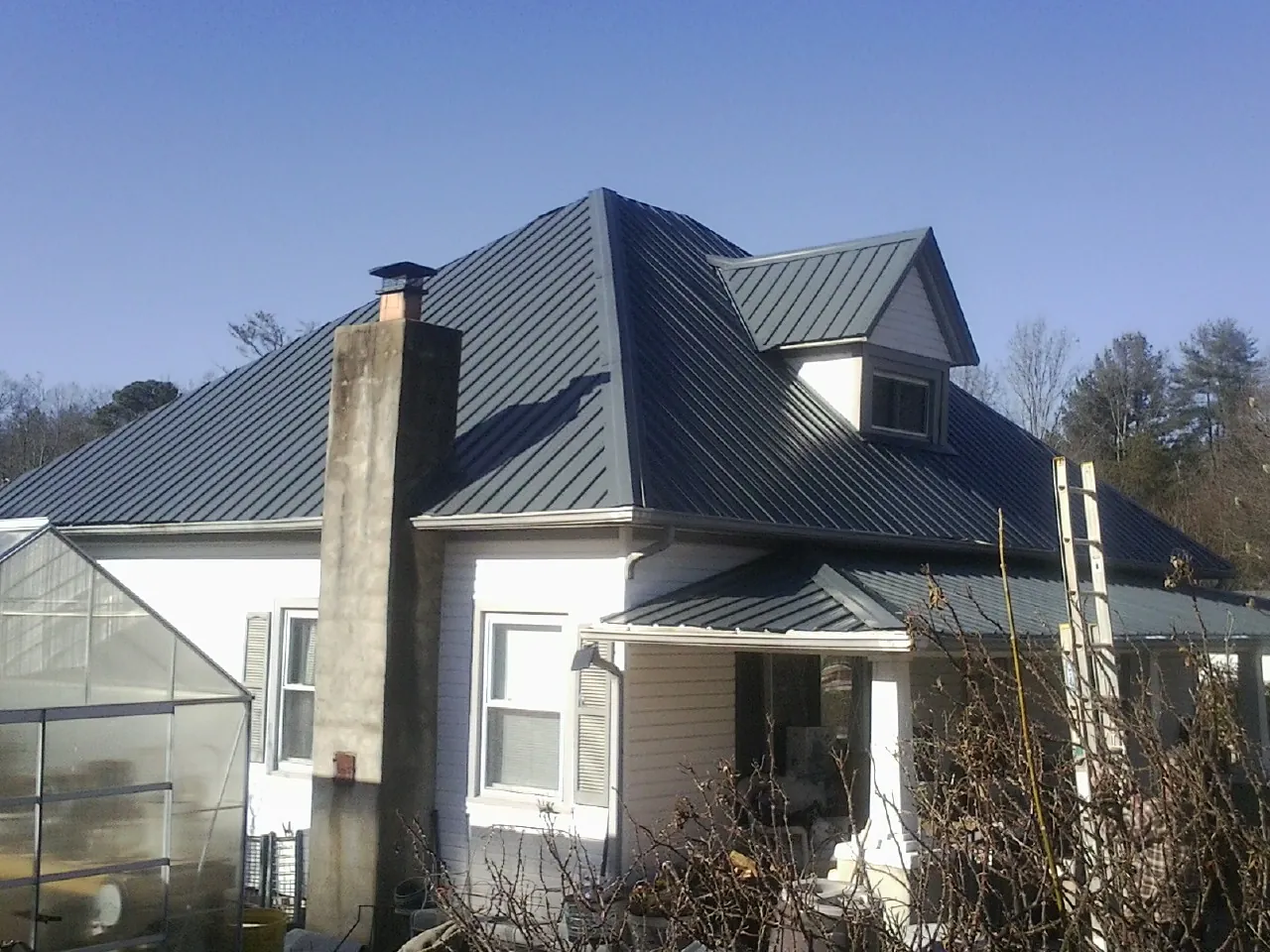 Dark blue standing seam metal roof on a white farmhouse with dormer — Slate & Tile Roof Repair by Roofing Brothers in Saint Lucas