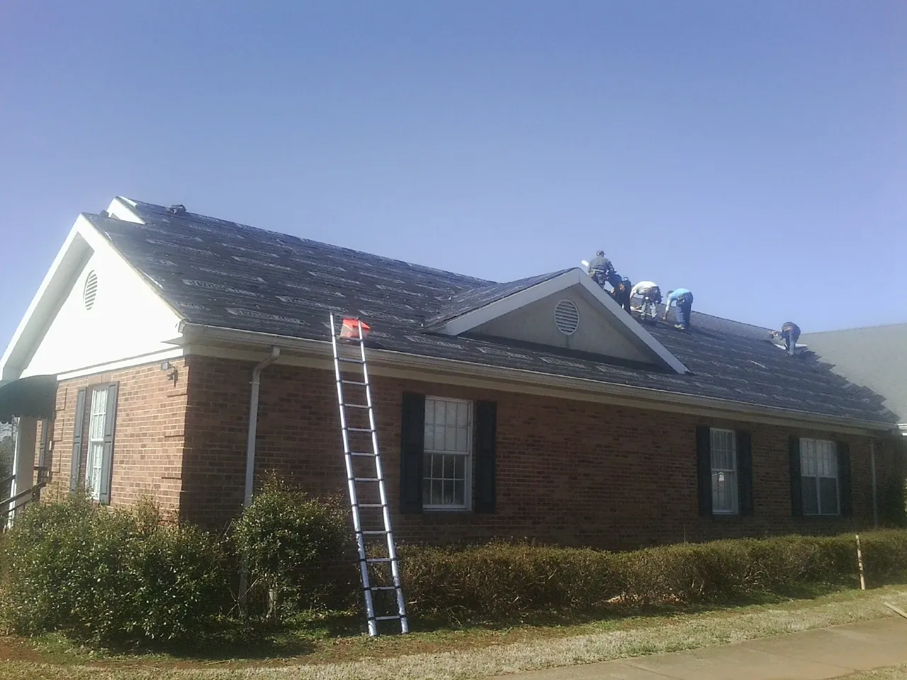 Crew tearing shingles off a brick ranch roof with a ladder set — Metal Roof Repair work by our crew in Saint Lucas