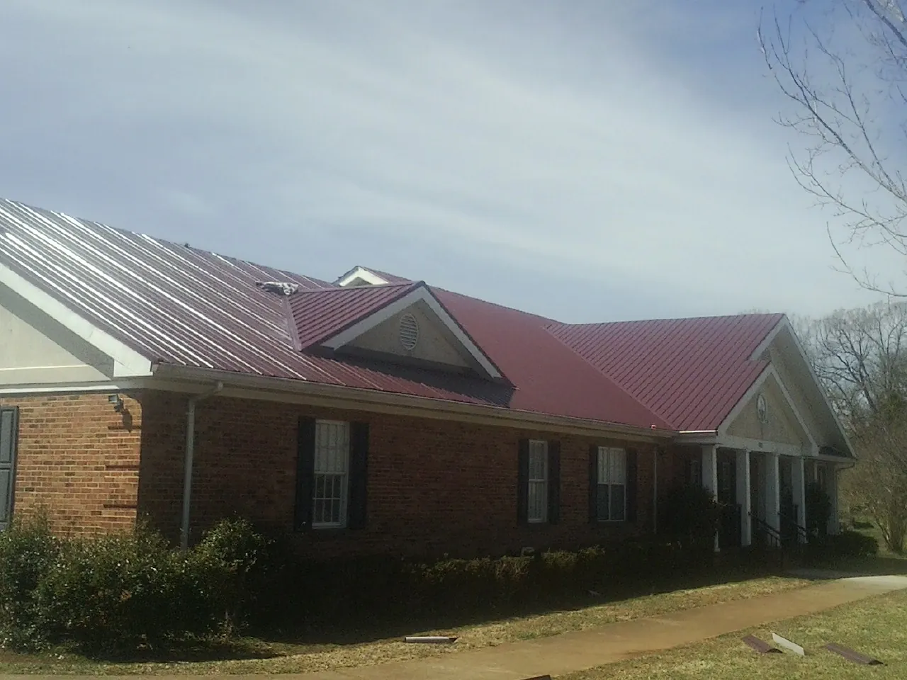Red metal roof with gabled entries on a long brick building, from a Hail Damage Roof Repair job in Saint Lucas