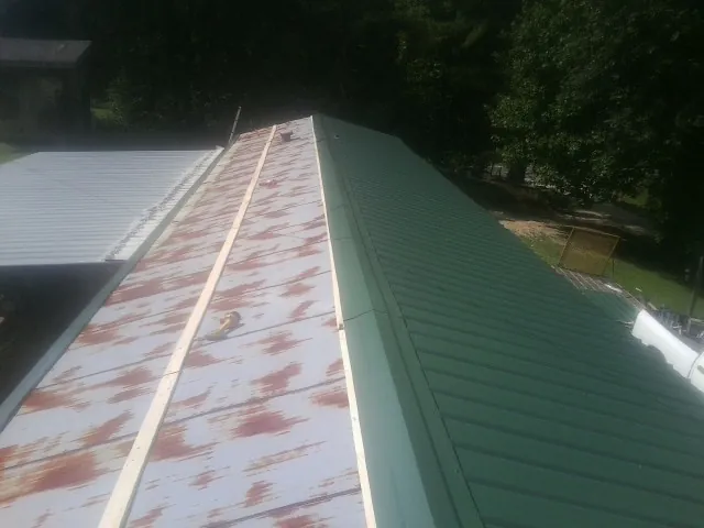Old rusted panels beside newly installed green metal roofing — Wind Damage Roof Repair by Roofing Brothers in Saint Lucas