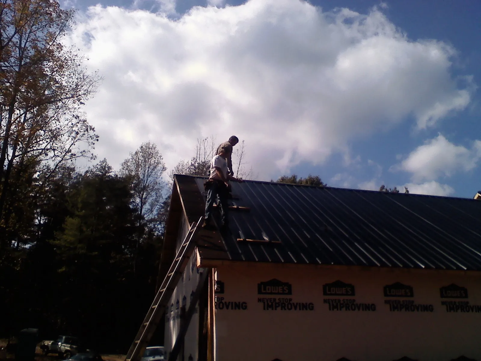 Roofer fastening dark metal panels high against a cloudy sky, from a Roof Inspection job in Saint Lucas