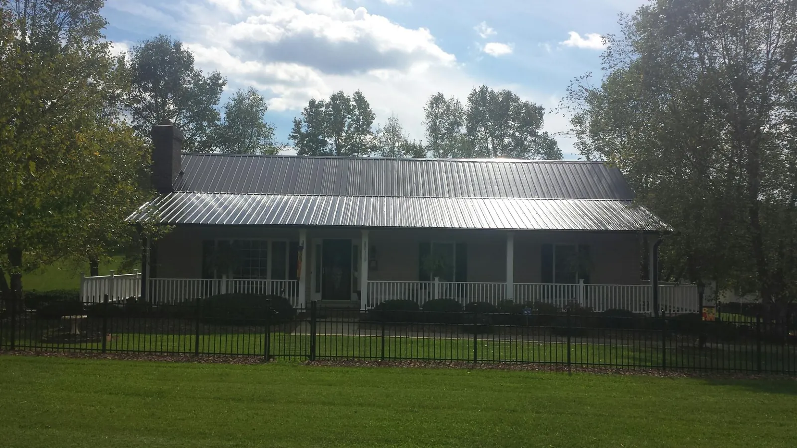 Gray metal roof on a brick ranch with a full width front porch — Gutter Guard Installation work by our crew in Saint Lucas