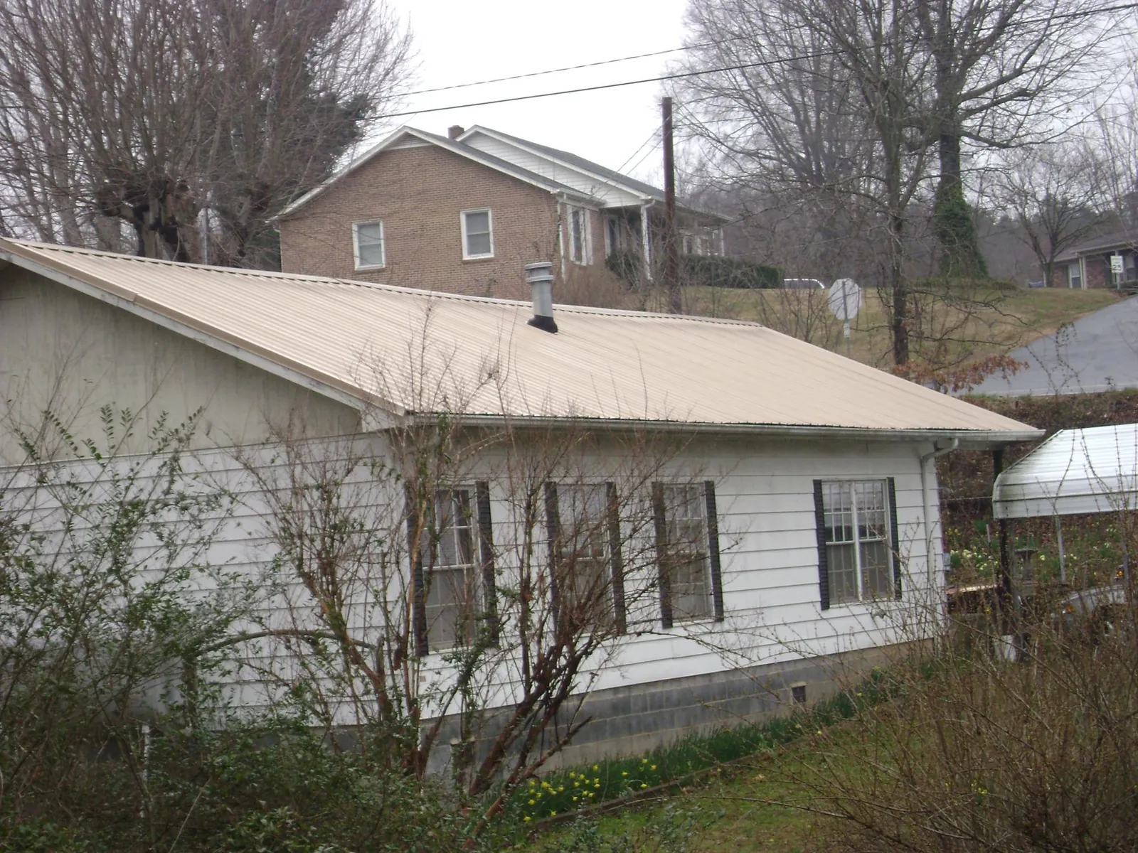 Tan metal roof on a white sided house set into a hillside — Commercial Roofing by Roofing Brothers in Saint Lucas