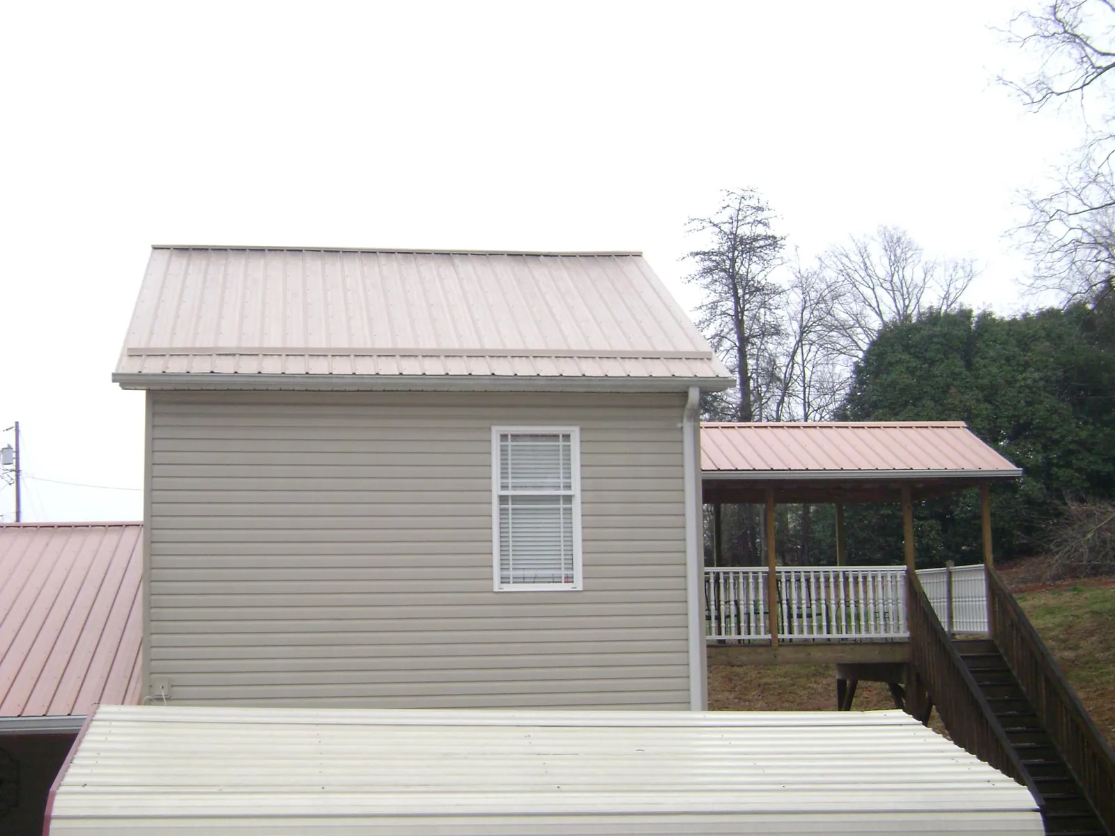 Tan metal roofs on a two story addition and attached porch, from a Roof Replacement job in Saint Lucas